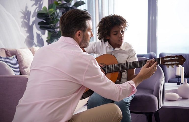 A teacher shows a student how to place their fingers on the fretboard of a C40 acoustic guitar.