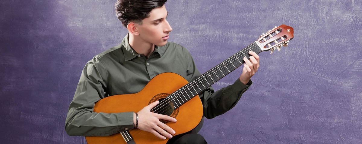 Person sitting on a stool playing a C40 acoustic guitar. Text reads Rising to excellence, one step at a time.