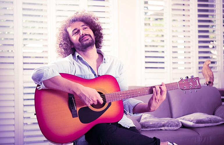 Man looking up while playing an F310 Cherry Sunburst acoustic guitar in his living room on his couch.