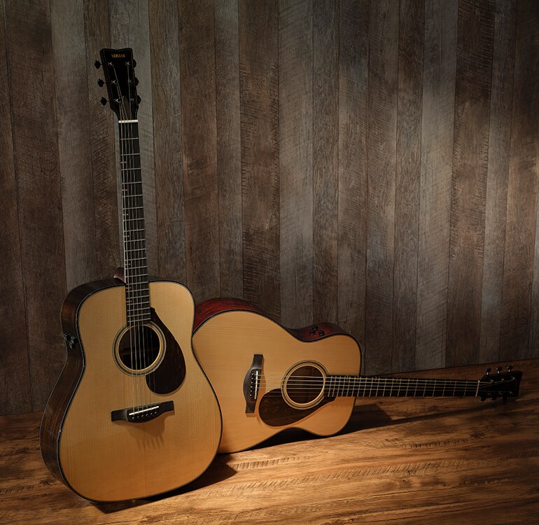 A FG9 RX and a FS9 MX are lined up on a wooden floor, showcasing the differences in their body shapes and types of wood used. The FG9 RX is standing upright on the left, while the FS9 MX is lying down on the right.